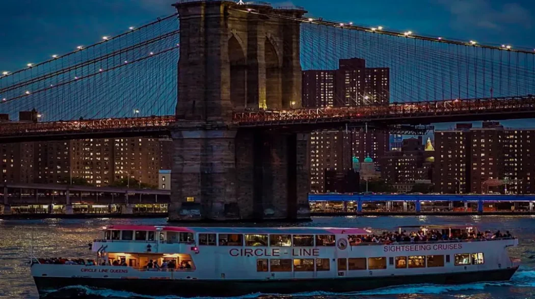 The Circle Line cruise sailing under the Brooklyn Bridge at night